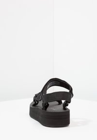 Sandales à plateforme noires avec brides ajustables, semelle intérieure texturée et semelle extérieure en caoutchouc épais. Design simple, adapté à un usage décontracté.