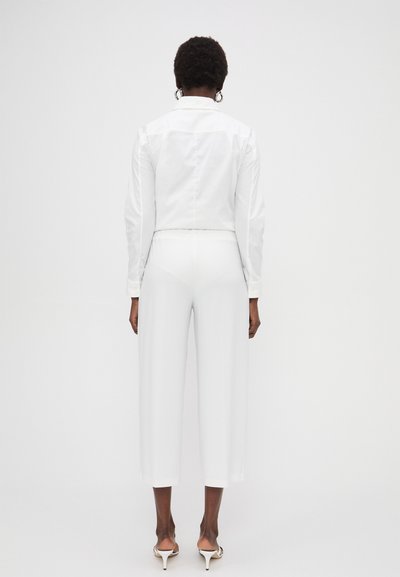 Weißer, taillierter Blazer mit langen Ärmeln, kombiniert mit weit geschnittenen weißen Hosen. Glattes, leichtes Material mit subtiler Optik. Klassische Knopfdetails.