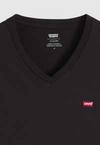 Fekete pamut póló V-nyakú kialakítással. Bal oldalon egy kis piros Levi's logó látható. Címke, rajta ápolási utasításokkal, látható.