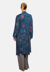 Blue floral kimono with vibrant embroidery, long sleeves, and a tie belt. Paired with striped wide-leg pants.