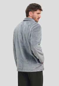 Chaqueta de corduroy gris con una textura suave, con diseño de cuello y bolsillos laterales. Costuras visibles y dobladillo recto.