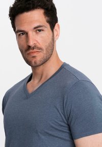 T-shirt grigia a scollo a V realizzata in tessuto morbido, con maniche corte e vestibilità comoda, presentata su un modello con uno sfondo neutro.