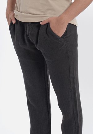 Pantaloni in lino neri con vestibilità ampia, tasche laterali e una texture liscia. Progettati per il comfort con dettagli minimalisti.