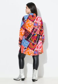 Kleurrijke jurk met een patroon in levendige oranje, roze en blauwe ontwerpen. Gecombineerd met zwarte leggings en zilveren enkellaarsjes.