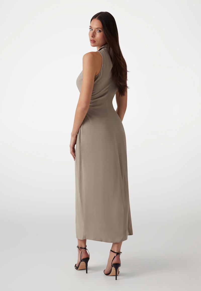 Abito maxi beige senza maniche con scollatura alta, texture liscia e silhouette aderente. Indossato con sandali neri con tacco alto e cinturini.