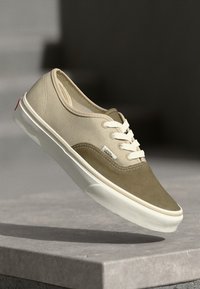 Sneaker din pânză bej și suede verde măsliniu, cu șirete albe și talpă din cauciuc, având un eticheta cu logo pe lateral și detalii de cusătură maro.