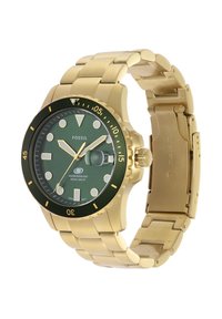 Montre Fossil en ton or avec un cadran vert, un boîtier rond, des index lumineux et un bracelet en métal doré. Étanche jusqu'à 100 mètres.