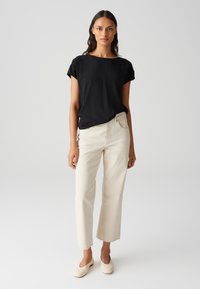 Maglietta nera a maniche corte con scollatura rotonda, abbinata a pantaloni ampi color crema. Tessuto dalla superficie liscia e taglio cropped con dettagli a orlo sfrangiato.