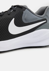 Baskets de sport noires et grises avec tige en mesh, logo swoosh blanc, accents texturés et semelle intermédiaire blanche. Design bas et col rembourré.