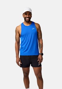 Blå sporttopp med rund hals och logotyp, kombinerad med svarta shorts. Tillbehör inkluderar en vit keps och en svart klocka.