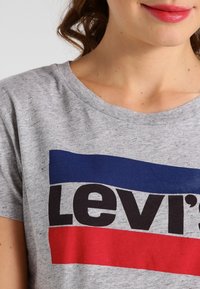 Gray cotton t-shirt displaying "Levi's" logo in black, with horizontal navy and red stripes above and below the text. Classic crew neck.
