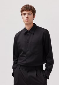 Schwarzes Langarmhemd mit Knöpfen und Kragen, einer einzelnen Brusttasche, glatter Textur und passend zu einer schwarzen Hose.