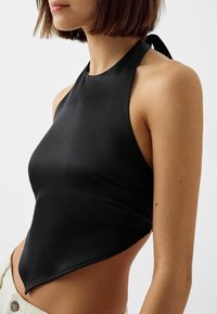 Svart satin halterneck-top med en triangulär fåll, slät textur och knutet nackband. Har en minimalistisk design och sidoklipp.