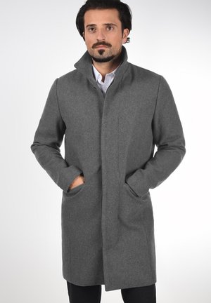 Abrigo de lana gris con un alto cuello, bolsillos laterales y un diseño aerodinámico, que presenta una textura suave y un ajuste a medida.