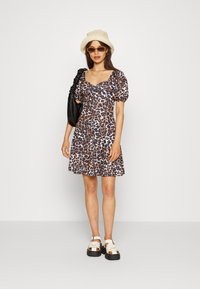 Vestido com padrão de leopardo, mangas bufantes, corpete ajustado, saia rodada e decote quadrado. Combinado com um chapéu de aba larga e sandálias chunky.