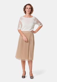 Fleeced beige rok met een luchtige, semi-doorschijnende witte top met kantdetails op de korte mouwen en decoratieve accenten op de halslijn.