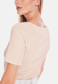 Short-sleeve beige top with a wide neckline and soft cotton texture. Features raglan sleeves and a simple design without embellishments.