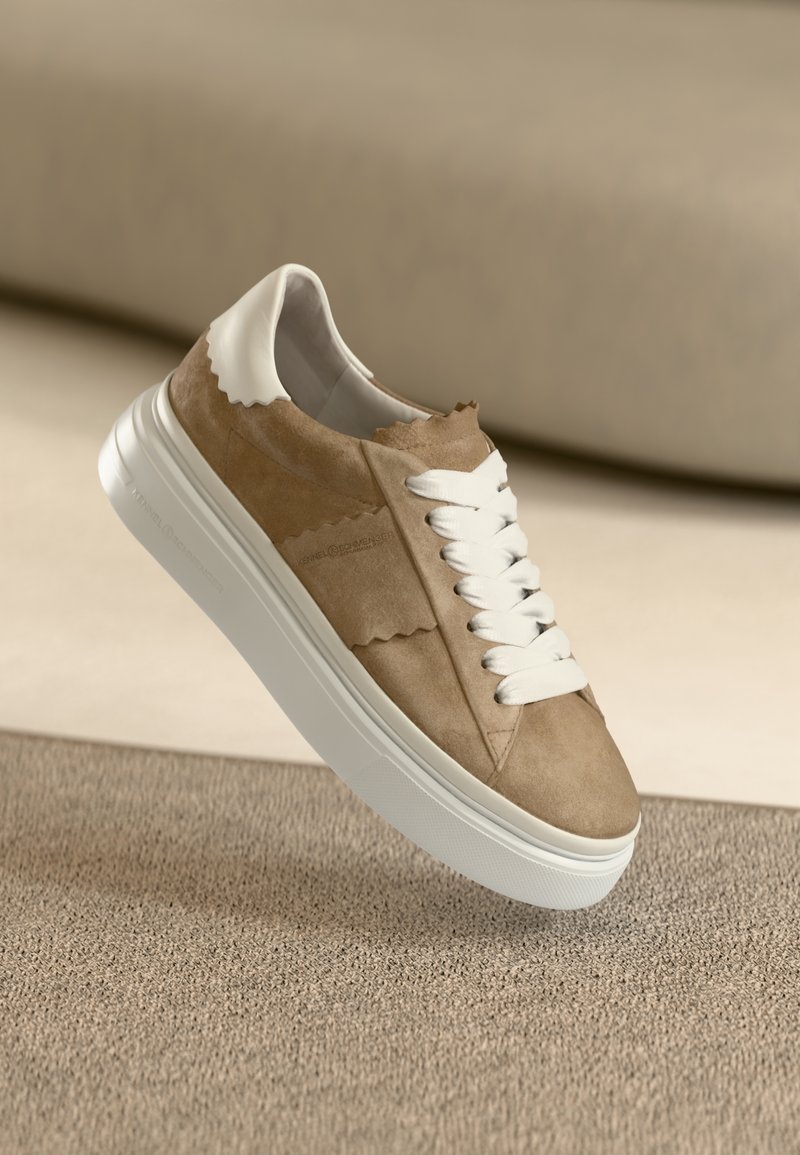 Μπεζ σουέντ αθλητικό παπούτσι με λευκή λαστιχένια σόλα, διαθέτει λευ κά κορδόνια και σχεδιασμό με κυματοειδή άκρη στον αστράγαλο. Μαλακή υφή, μινιμαλιστικό στυλ.