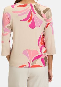Beige top with three-quarter sleeves featuring a colorful floral pattern in pink, red, and brown. Smooth knit fabric with ribbed cuffs.