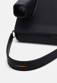 Black camera with a rectangular lens, textured surface, and a black leather strap featuring a multi-colored accent stripe.