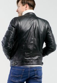 Zwarte leren jas met een gestructureerde afwerking, voorzien van een hoge kraag, gewatteerde schouders, zijritsen en een verstelbare riem in de taille.