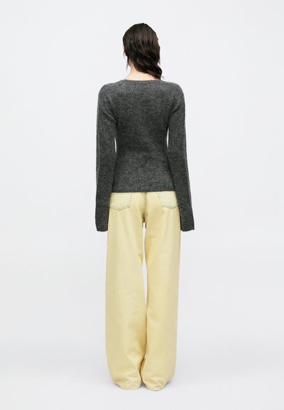 Pulover gri tricotat cu mâneci lungi, asortat cu pantaloni evazați din denim galben deschis. Materialul pare moale și texturat.