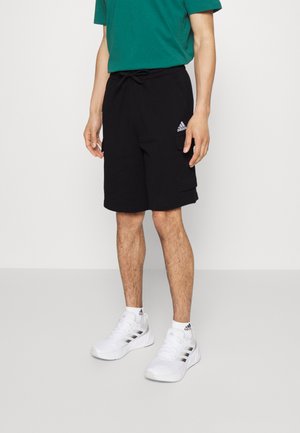 Shorts neri di cotone con vita regolabile e tasche laterali, con un piccolo logo Adidas bianco sulla coscia sinistra. Indossati con sneakers bianche.