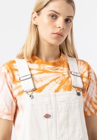 Hvite overaller med metallklips, kombinert med en oransje og hvit tie-dye t-skjorte. Inneholder merkeetiketter på begge plaggene. Jevn stoffstruktur.