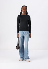 Black long-sleeve top with a square neckline, paired with light blue flared jeans and white sneakers, holding a small dark handbag.