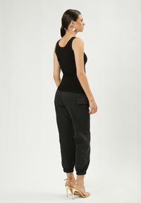 Top fitted senza maniche nero, abbinato a pantaloni taper neri con tasche laterali. Tacchi dorati con cinturini completano il look.