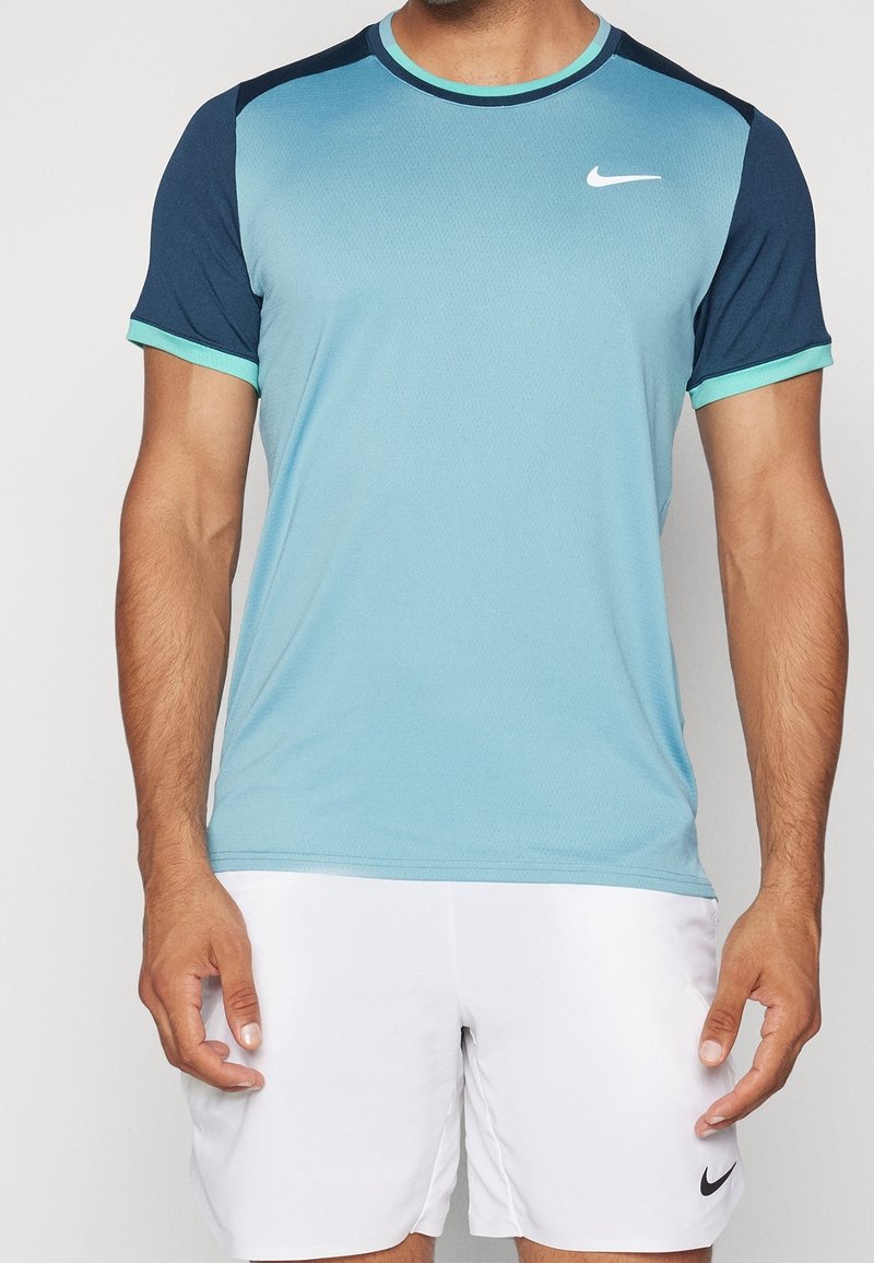 Camiseta atlética de manga corta en azul claro con hombros en azul oscuro y acentos en turquesa. Hecha de un tejido transpirable, presenta un logo de Nike.