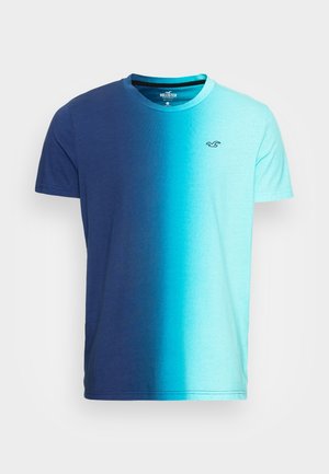 Koszulka z krótkim rękawem, z okrągłym dekoltem, w gradientowych odcieniach niebieskiego, od ciemnego granatu do jasnego turkusu, z małym logo mewy na klatce piersiowej.