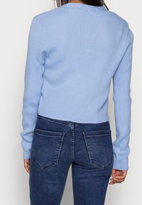 Ljusblå rippad tröja med långa ärmar, figurnära design, rund halsringning, bärs tillsammans med mörkblå raka jeans med bakfickor.