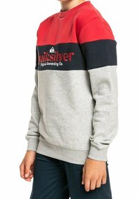 Sudadera con sección superior roja, banda central azul marino y sección inferior gris. Tejido suave con puños de canalé y detalle de logotipo bordado.