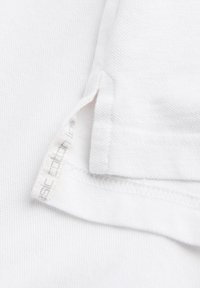 Biała bawełniana tkanina o teksturowanym splocie. Posiada przeszyty brzeg oraz metkę z napisem "podstawowa bawełna". Gładka powierzchnia, bez wzorów i akcentów.