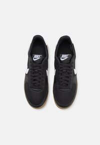 Sorte atletik sko med en glat syntetisk overdel, hvidt Nike-logo, sorte snørebånd og sål af brunt gummi. Designet har en klassisk lav profil.