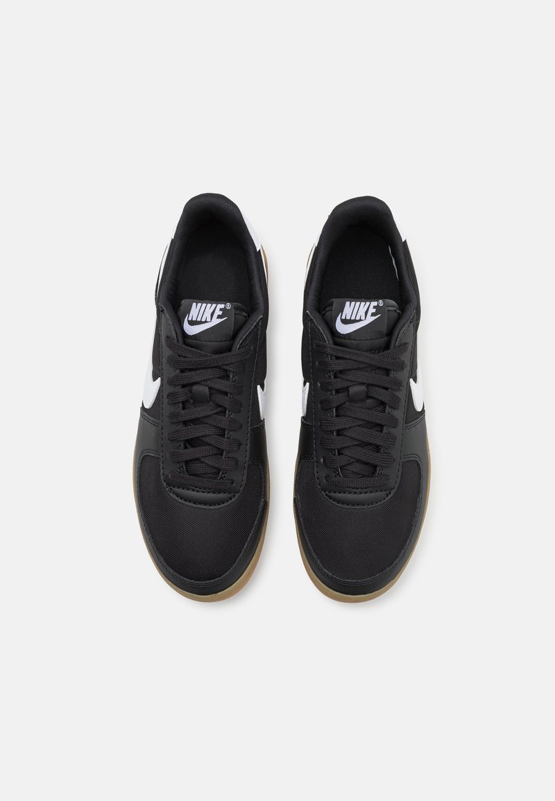 Baskets noires de sport avec un dessus en synthétique lisse, logo Nike blanc, lacets noirs et semelle en caoutchouc marron. Le design présente un profil bas classique.