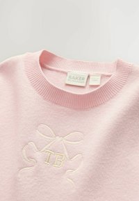 Svetloružová mikina vyrobená z mäkkej látky, s rebrovaným golierom a vyšívaným dizajnom mašle so stredom označeným "TB".