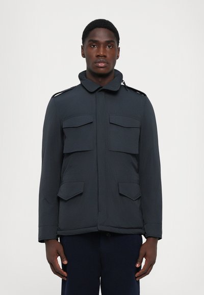 Giacca da uomo di un blu navy scuro con colletto alto, quattro tasche frontali, spalline e una texture morbida e leggera.