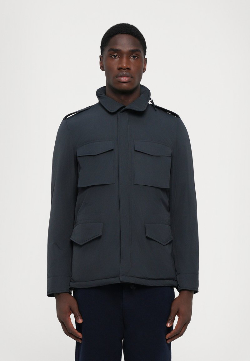Chaqueta oscura de marina para hombre con un alto cuello, cuatro bolsillos en la parte frontal, hombreras y una textura suave y ligera.