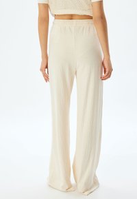 Lichte, crèmekleurige, wijde broek met een textuurstof. Beschikt over een elastische tailleband en een ontspannen pasvorm.
