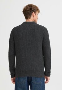 Mørk grå strikket genser med et teksturert mønster, med lange ermer og rund krage, vist fra baksiden. Uformell design, ribbede mansjetter.
