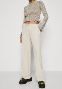 Světle béžové široké kalhoty s elastickým pasem, spárované s texturovaným pleteným krátkým topem v tlumených barvách a platformovými černými botami.