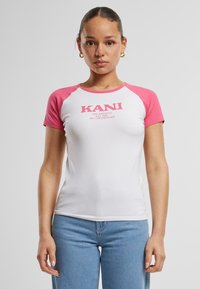 T-shirt blanche avec des manches raglan roses, arborant un logo imprimé "KANI" sur le devant, fabriquée en coton doux.