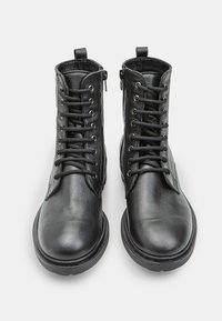 Stivali neri in pelle con punta arrotondata, con lacci davanti e cerniera laterale. Presentano pelle testurizzata e una robusta suola in gomma.