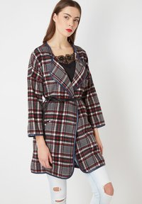 Abrigo de cuadros gris con acentos en rojo y negro, hecho de tejido suave. Presenta un cuello chal, cintura ceñida con cinturón y dos bolsillos.