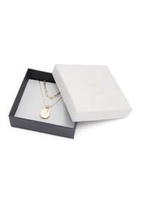 Collier en plusieurs couches en ton or avec un pendentif texturé, présenté dans une boîte noire doublée de suède gris avec un couvercle texturé blanc et un logo.