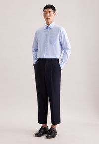 Jasnoniebieska koszula w kratę z kołnierzykiem zapinanym na guziki, zestawiona z ciemnogranatowymi plisowanymi spodniami i czarnymi sznurowanymi butami.