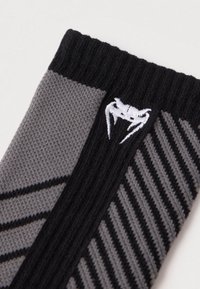 Pelēks un melns zeķes pāris ar ribotu aproci, fakturētu audumu un diagonālām joslām. Netālu no aproces izšūta baltā logo.