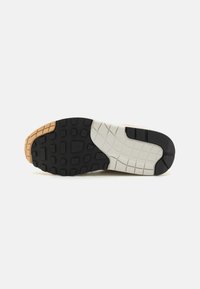 Sola de sapatilha em borracha com um padrão de piso multidirecional. Apresenta seções em preto, bege e branco. Texturizada para aderência e durabilidade.